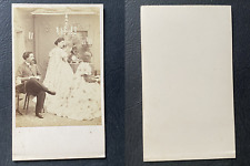 Three people in a living room, one man and two women in evening dresses, approx
